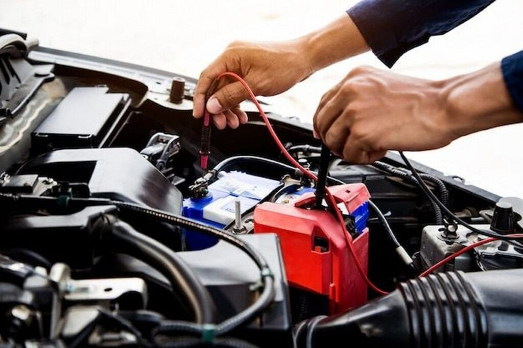 Auto mechanic using measuring equipment for checking car battery